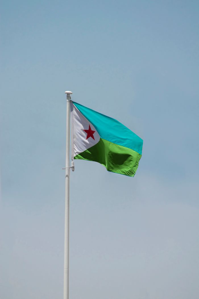 Photograph of the Djibouti national flag hoisted against a clear blue sky.